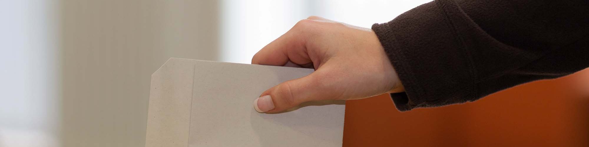 Person wirft einen Umschlag in eine Wahlurne