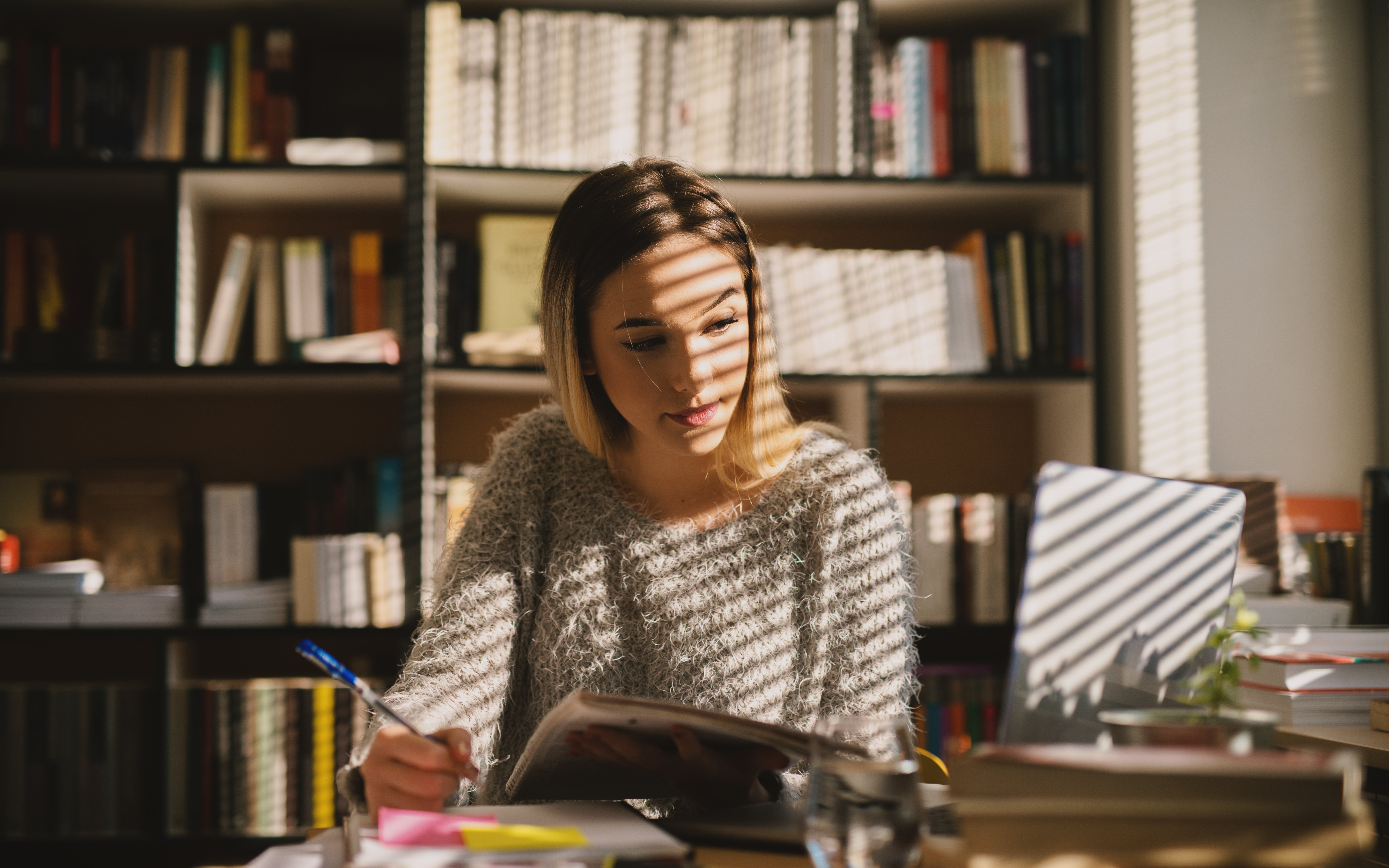 Eine junge Frau sitzt mit einem Stift in der Hand an einem Tisch und schaut auf einen Laptop. 