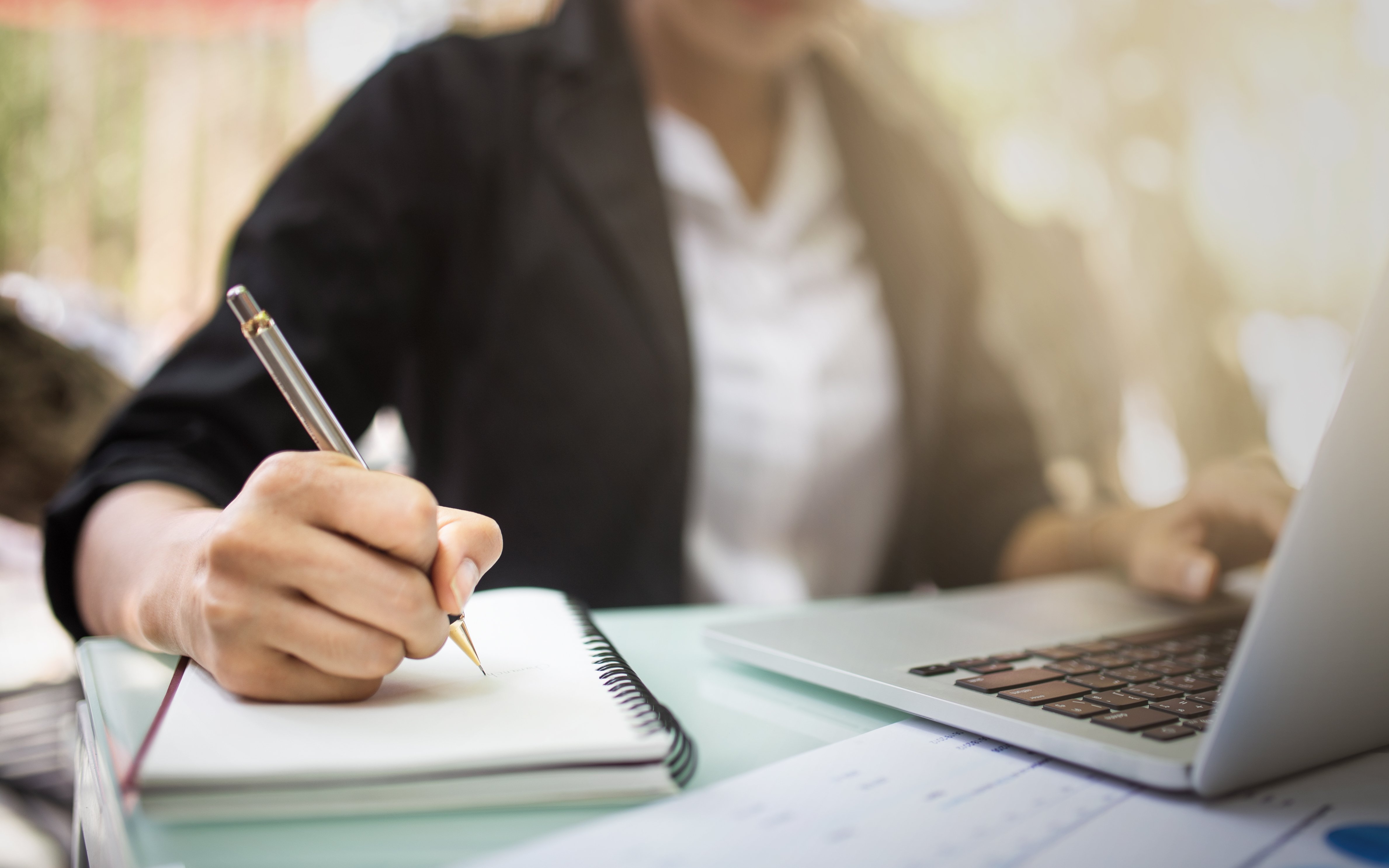 Frau am Schreibtisch schreibt in einen Notizblock Frau am Schreibtisch schreibt in einen Notizblock