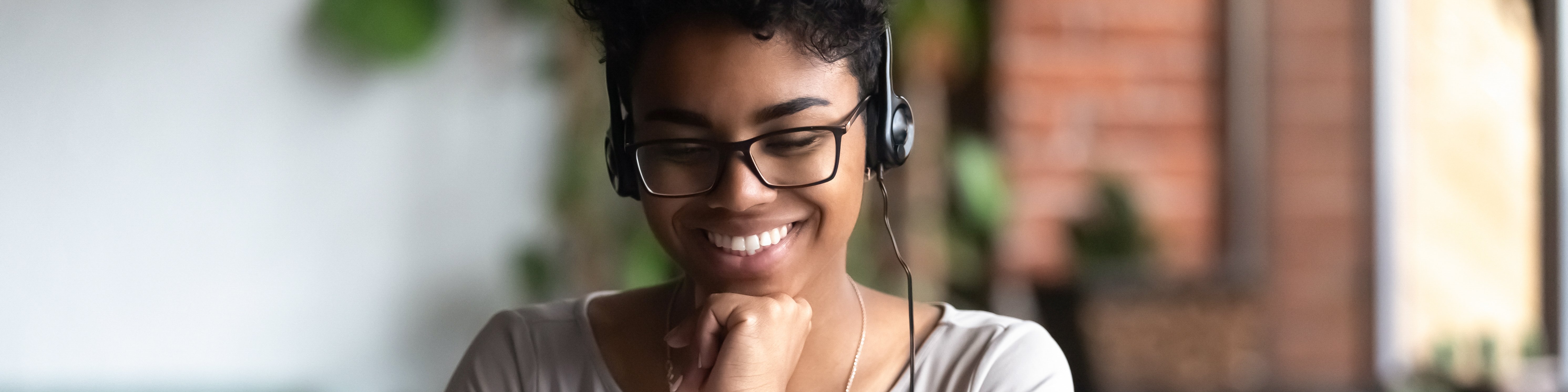 Eine junge Frau sitzt mit Kopfhören und einem Laptop am Schreibtisch