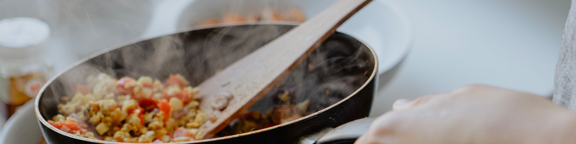 Person rührt mit einem Holzlöffel buntes Gemüse in einer Pfanne