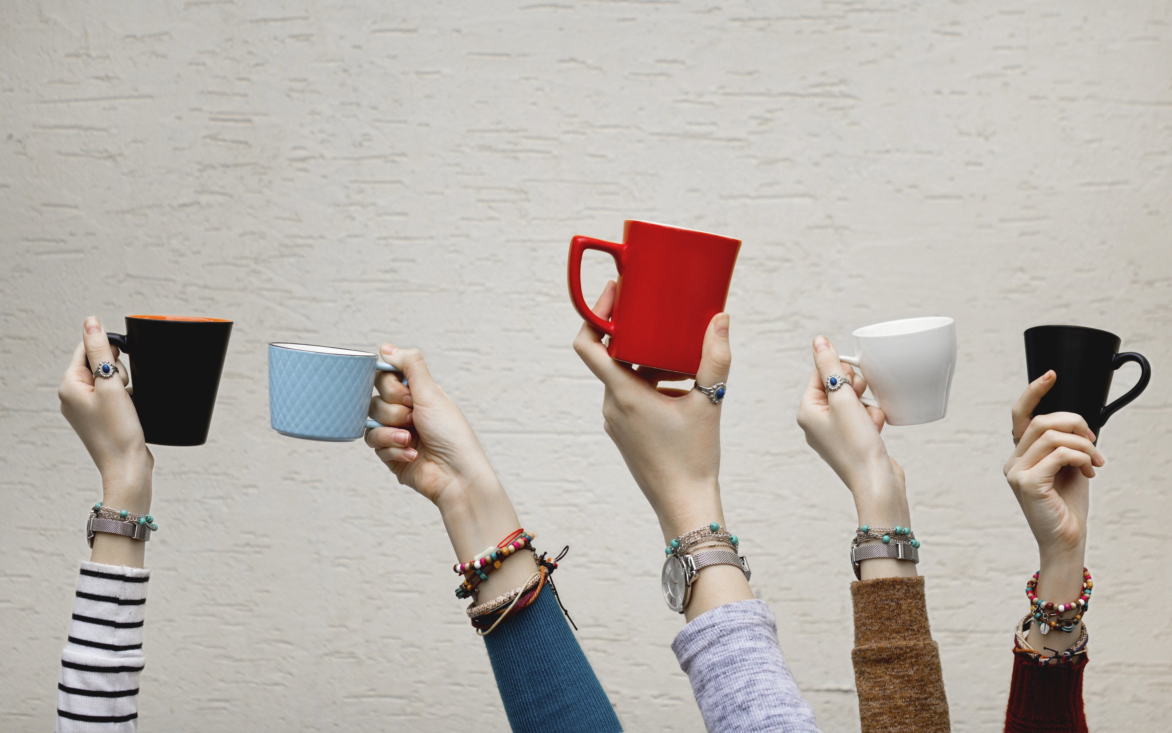 Fünf Hände halten jeweils eine Tasse in die Luft