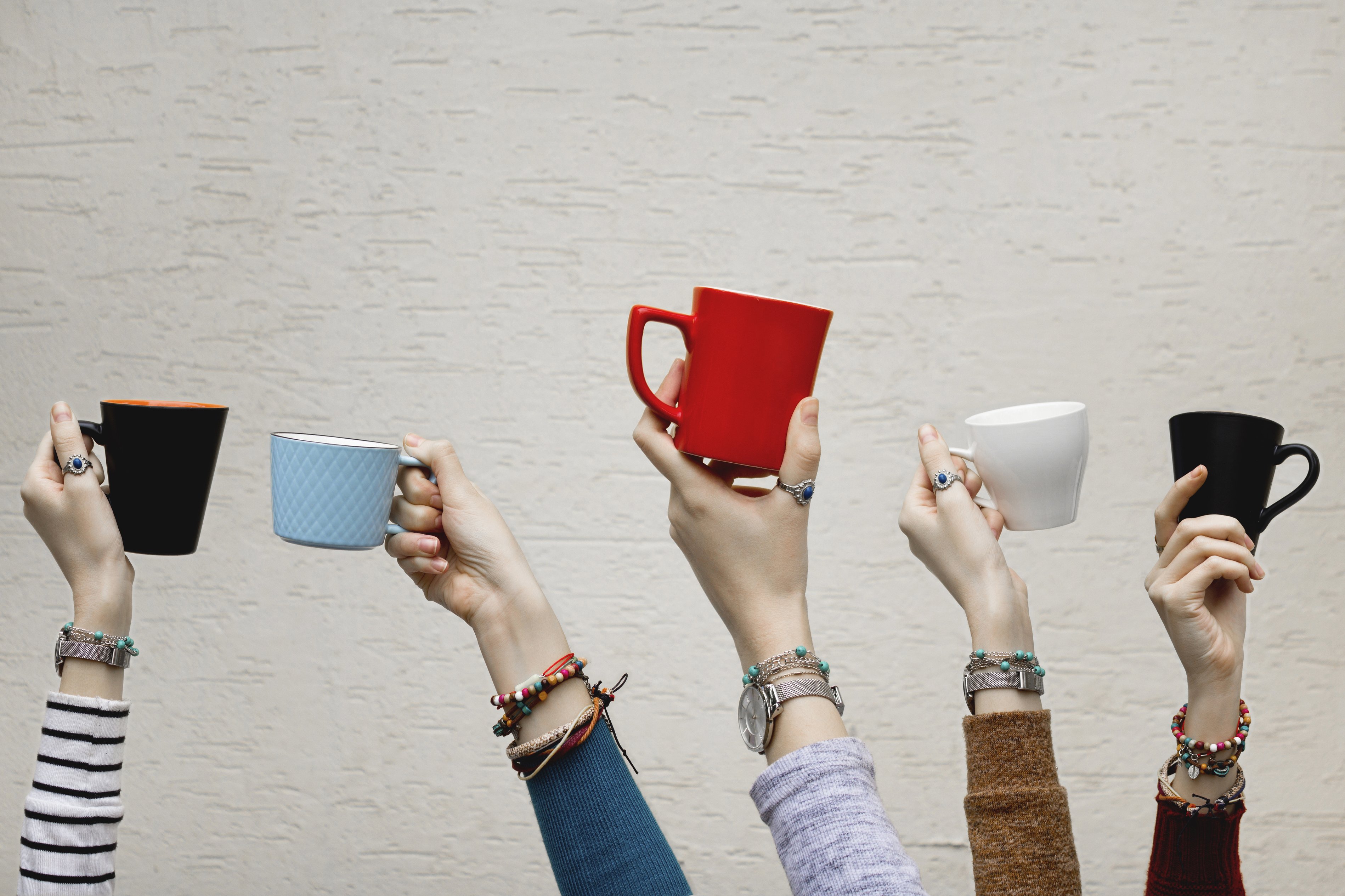 Fünf Hände halten jeweils eine Tasse in die Luft