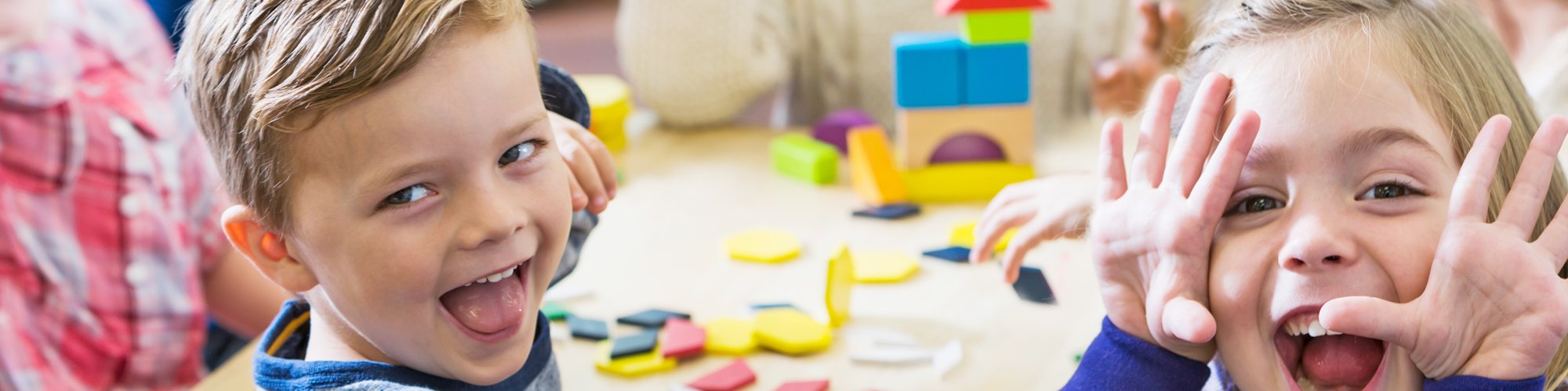 Children playing at a table in kindergarten, two children pulling faces