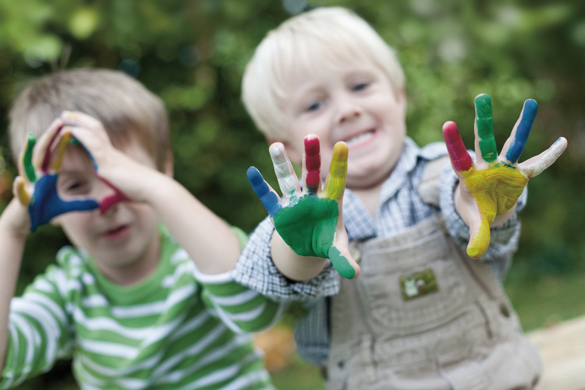 Two little boys stretch out their colorfully painted hands.