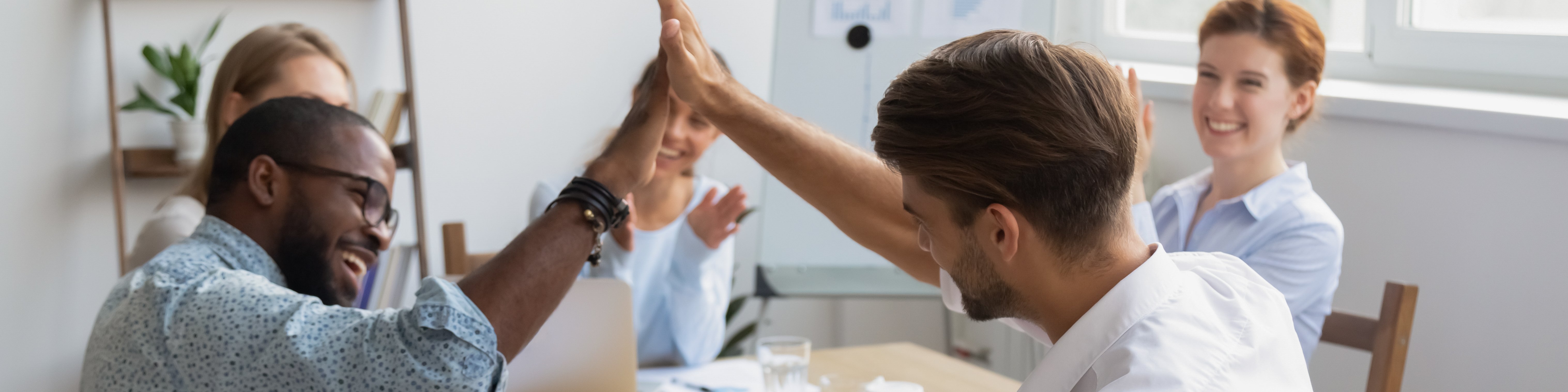 Five students are sitting at a table, two of them are giving each other a high five.