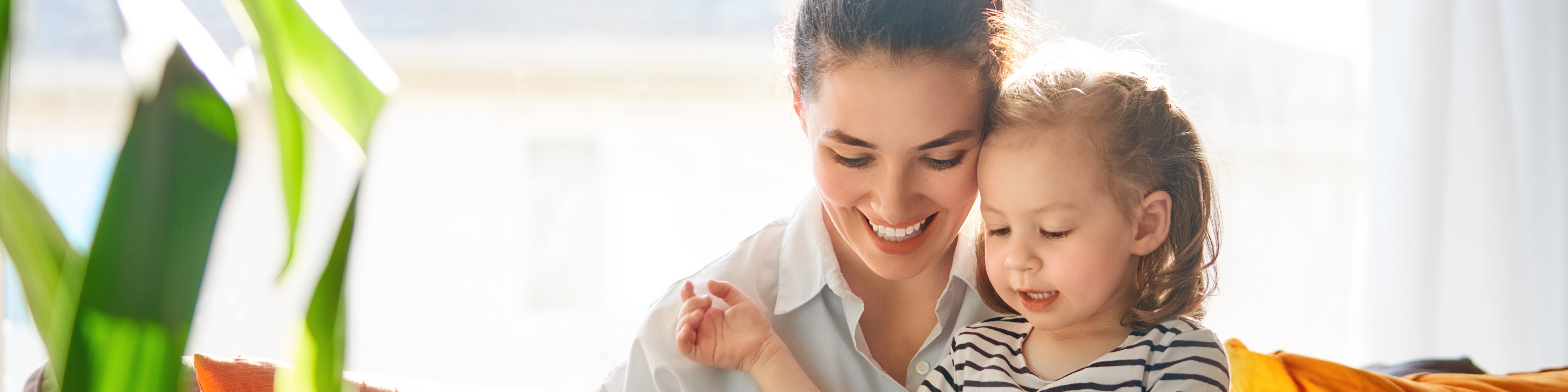 Junge Frau mit Tablet in der Hand sitzt mit kleinem Mädchen auf dem Schoß auf einer Couch