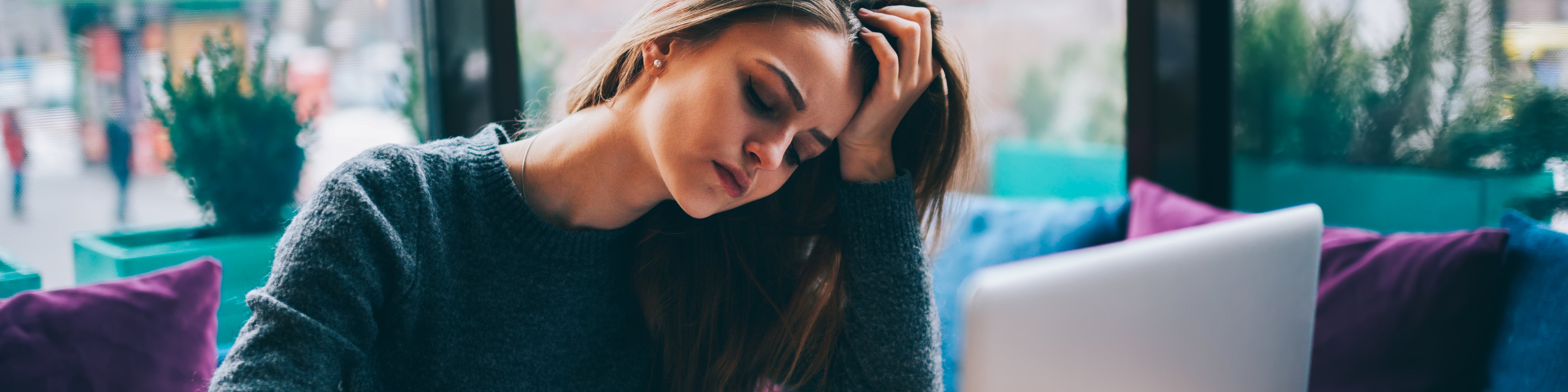 Junge Frau sitzt verzweifelt vor ihrem Laptop an einem Tisch
