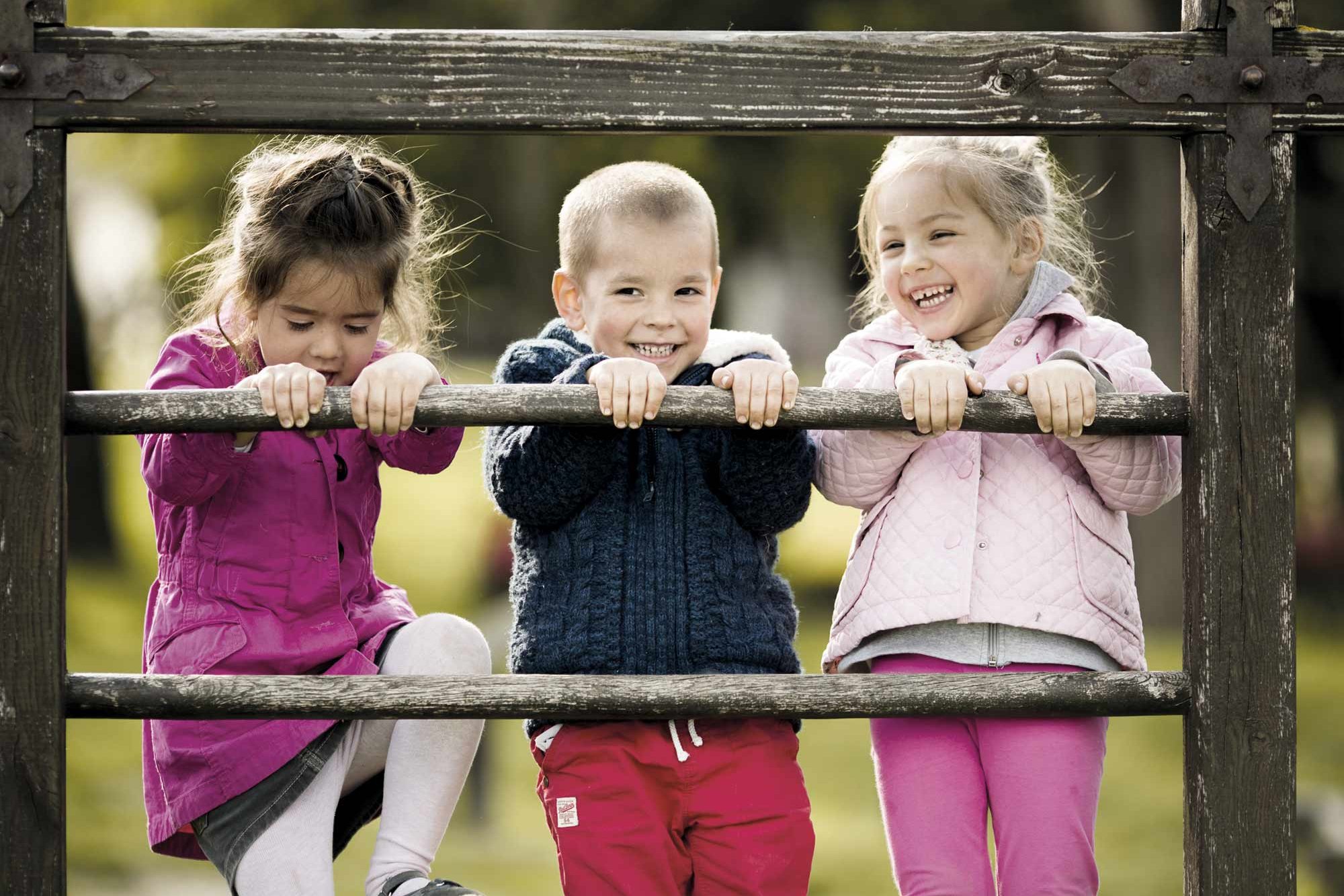 Three daycare children look through a wooden fence.