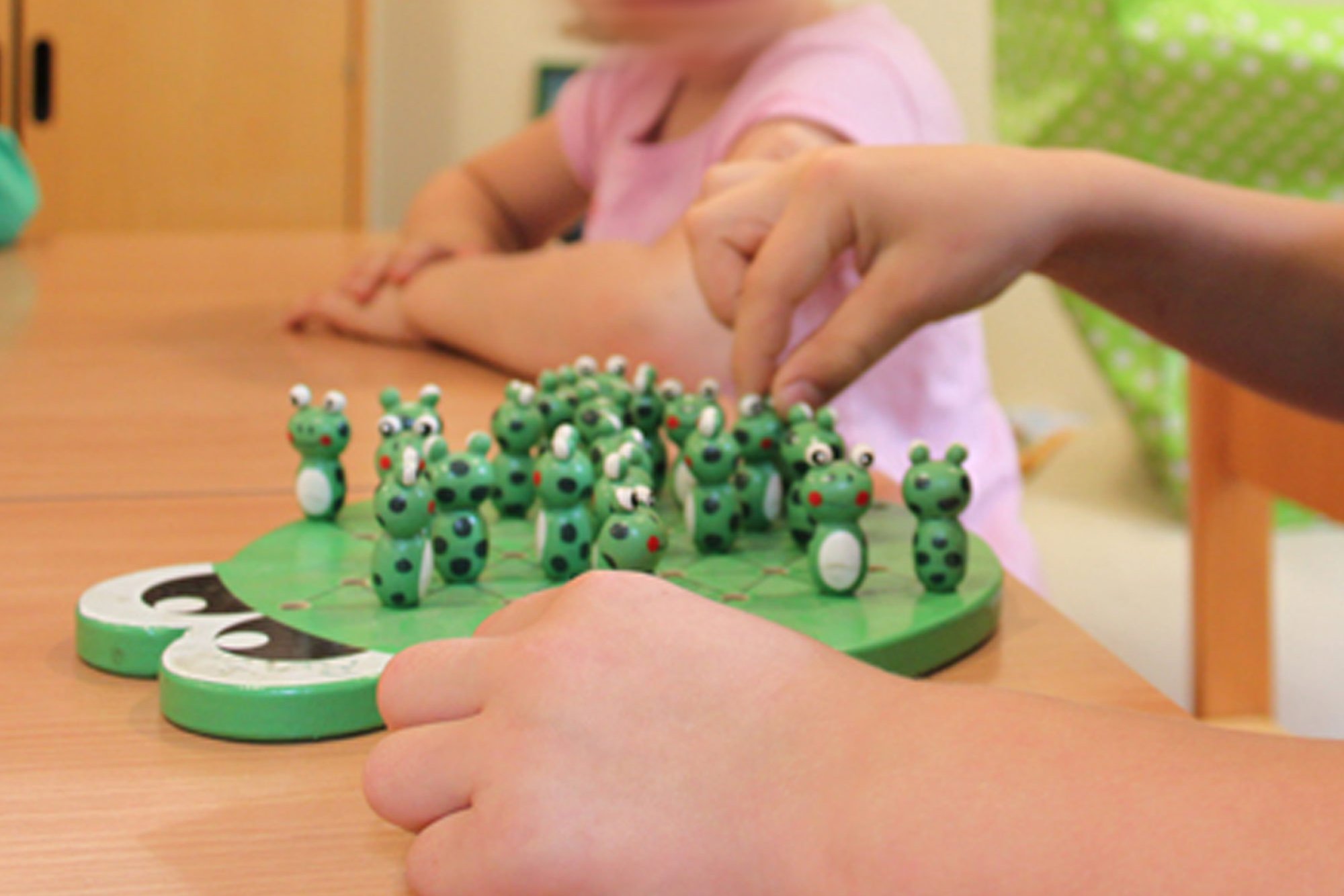 Two children are sitting at a table playing a frog game.